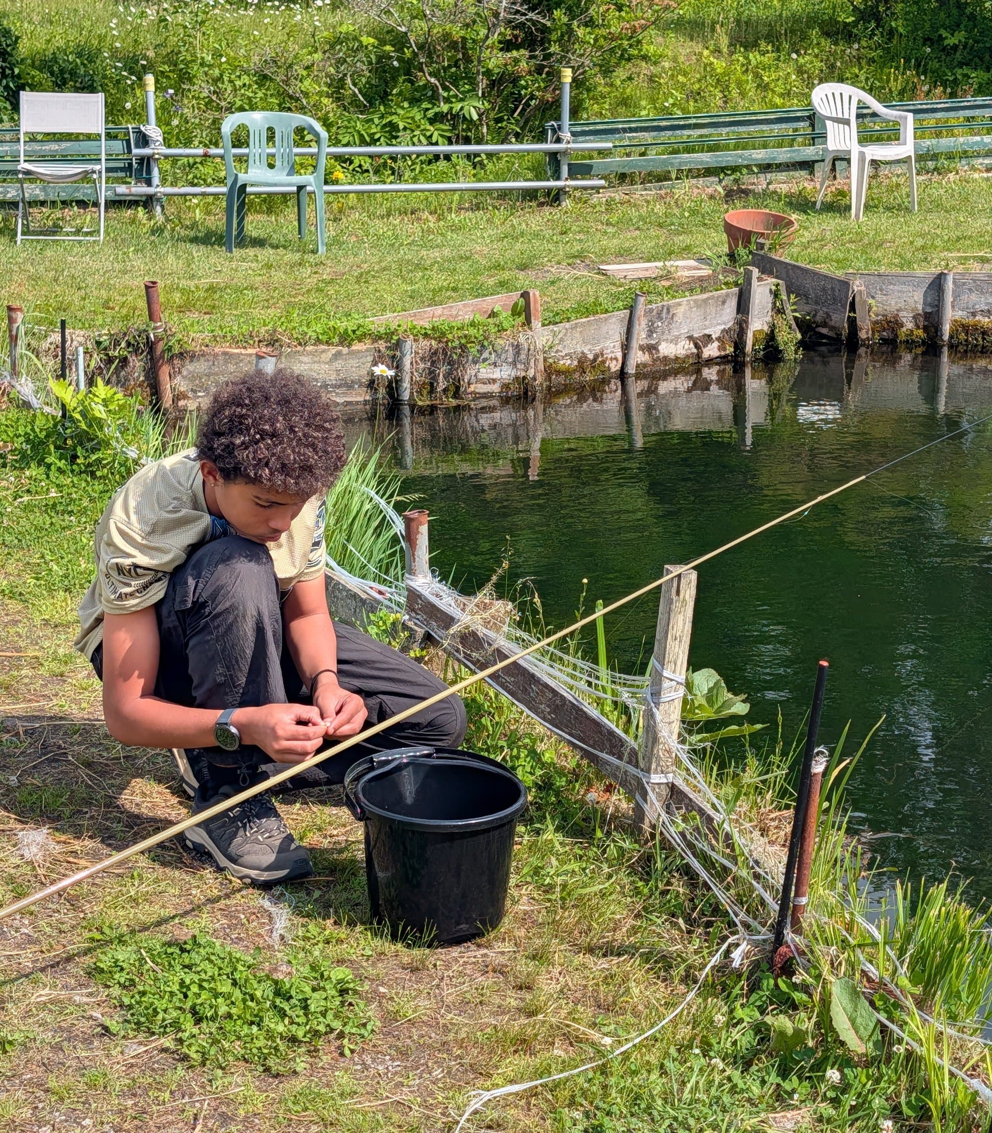 Reyaan crouched by a pond, tying a rig before fishing