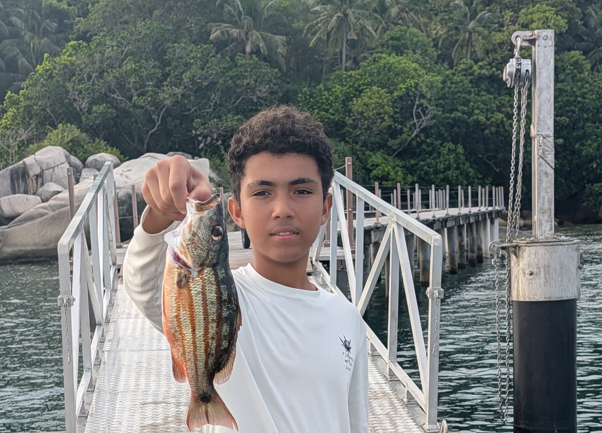 Reyaan holding up a fish on a dock, with palm trees in the background